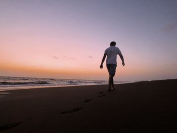 Rear view of man standing on beach during sunset