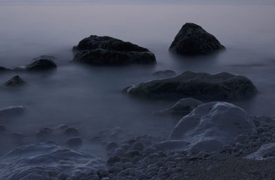 Rocks in sea against sky at dusk