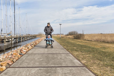 Grandfather pushing granddaughter in stroller on footpath