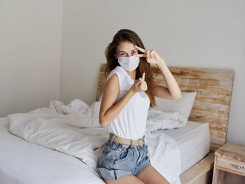 Portrait of young woman wearing mask sitting on bed at home