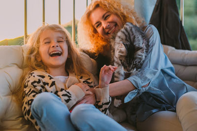 Happy child with smile plays on summer at home with mom, cat at sunset. cat, dog, pets family member