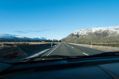 Road seen through car windshield against clear blue sky