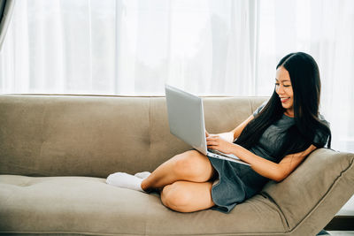 Young woman using laptop while sitting on sofa at home