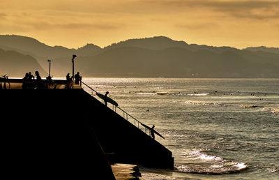 Silhouette people on beach against sky during sunrise