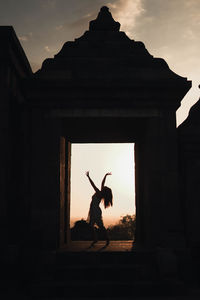 Silhouette woman with arms outstretched against sky at sunset