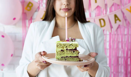  woman in party clothes preparing birthday table, celebrating and holding a piece of pistachio cake