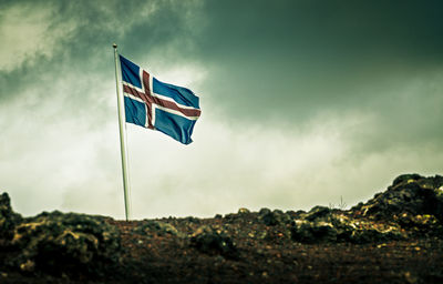 Low angle view of flag on rock against sky