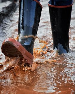 Low section of person wearing rubber boots walking in puddle