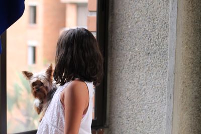 Side view of girl with dog standing by window at home