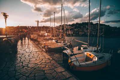 Boats moored in harbor at sunset