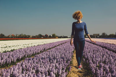 Woman walking in flower field against clear sky