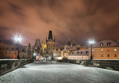 Illuminated street amidst buildings against sky at night