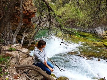 Man sitting on rock by river in forest