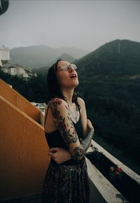 Young woman looking away while standing on railing against sky