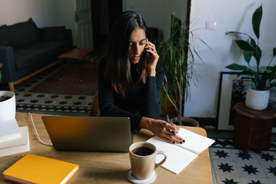 Young woman using mobile phone while sitting on table