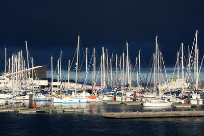 Sailboats moored on harbor against sky at night