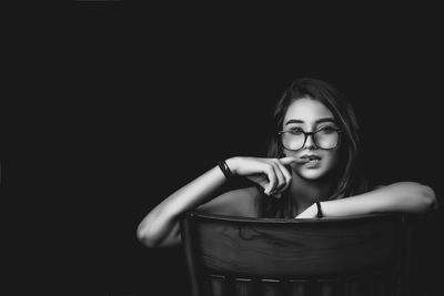 Portrait of young woman sitting on chair against black background