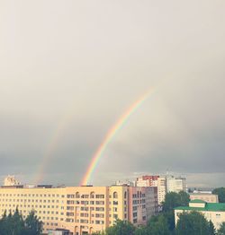 Rainbow over buildings in city against sky