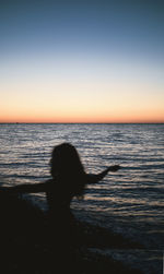 Silhouette woman standing on beach against sky during sunset