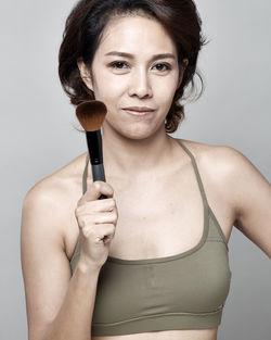 Portrait of smiling woman applying make-up with brush against gray background
