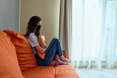 Side view of woman sitting on bed at home