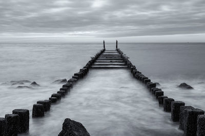 Wooden posts in sea against sky