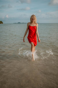 Rear view of young woman standing in sea against sky