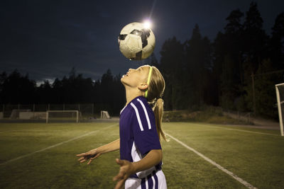 Side view of girl heading the ball on field against sky