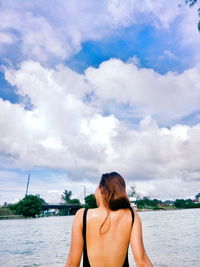 Rear view of woman standing by sea against sky