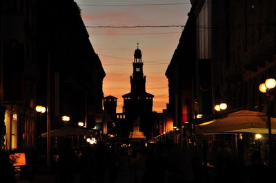 People on street against silhouette castello sforzesco during sunset in city