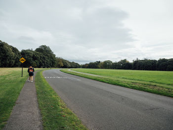 Rear view of man cycling on road amidst field against sky