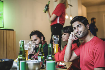 Portrait of young man sitting with friends while watching soccer at home
