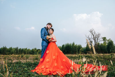 Newlywed couple embracing on field against sky
