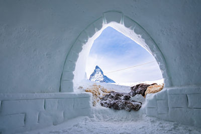 Snowcapped matterhorn peak against sky seen through entrance of igloo in alps