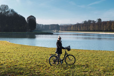 Rear view of man riding bicycle on lake against sky