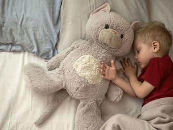 Close-up of boy sleeping with teddy bear on bed