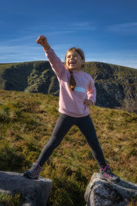 Young girl standing on two rocks with raised hand in triumph as she climbed mountain wicklow ireland
