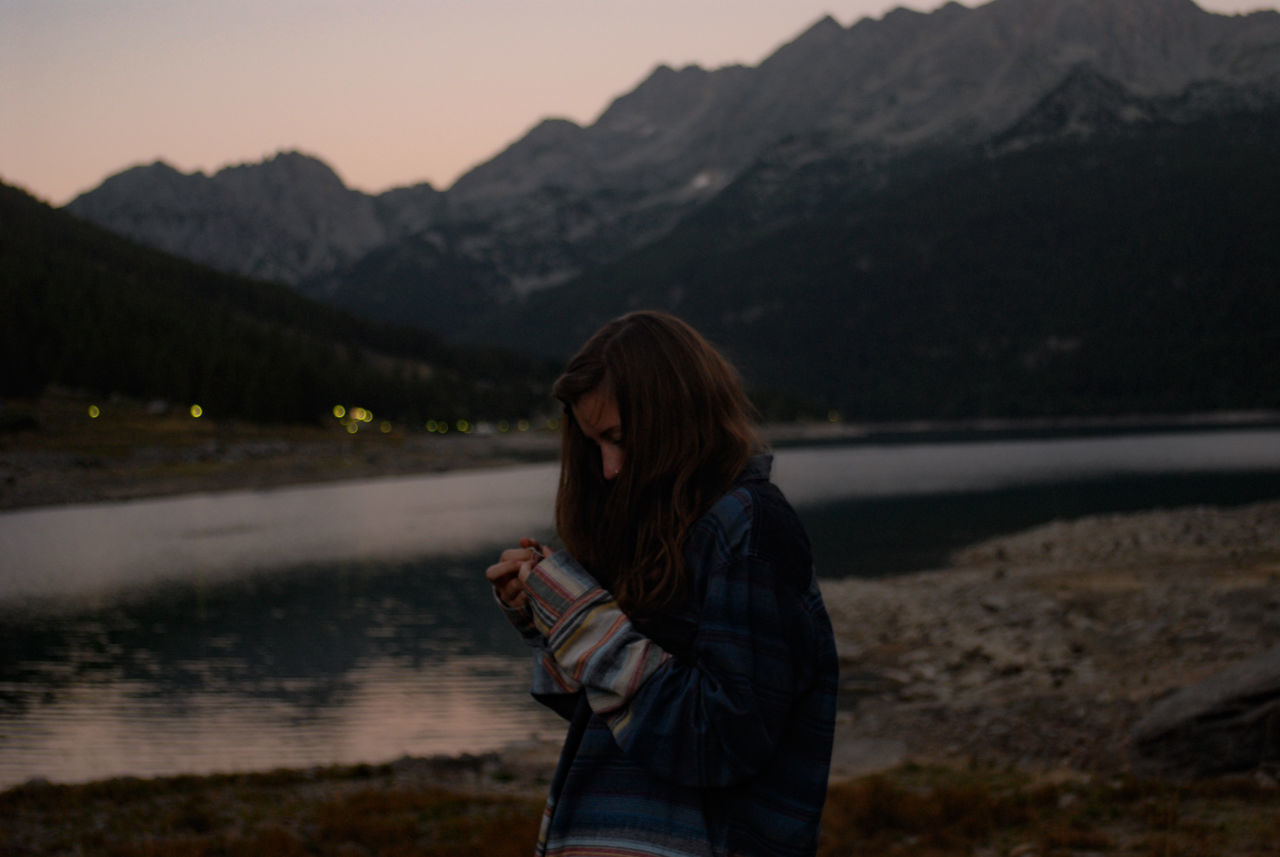 real people, one person, focus on foreground, standing, mountain, outdoors, nature, young women, young adult, holding, water, leisure activity, side view, sunset, lake, technology, day, wireless technology, beauty in nature, sky