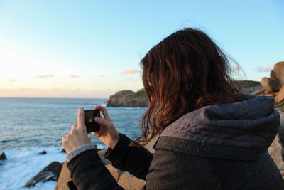 Rear view of woman photographing sea against sky