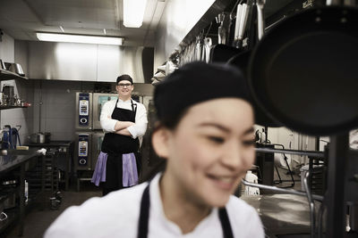 Portrait of confident male chef with colleague in foreground at commercial kitchen