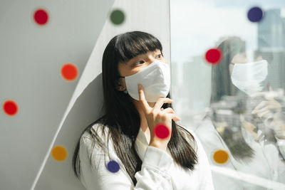 Woman wearing mask sitting by window at home