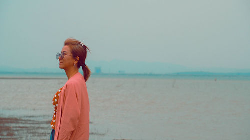 Side view of woman standing at beach against clear sky