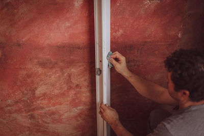 A handsome young caucasian man washes white window frames with a sponge and soap against a red wall