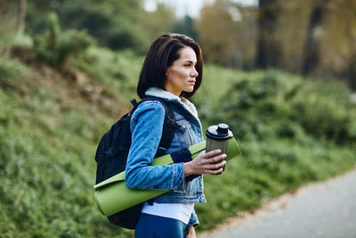Portrait of a beautiful young woman in nature with a fitness mat and a thermos for water.