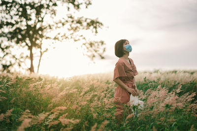 Girl on a spring meadow at sunset.  wears a dress and wide-brimmed hat. breathing through the mask.