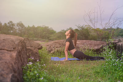 Side view of woman sitting on rock against sky