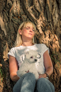 Woman with small dog is relaxing under a tree
