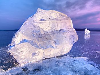 Shining wrinkled surface broken ice, fresh icy pieces on flat frost ground. colorful winter sunset.