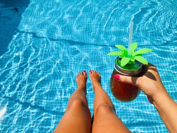 Low section of woman with drink in swimming pool