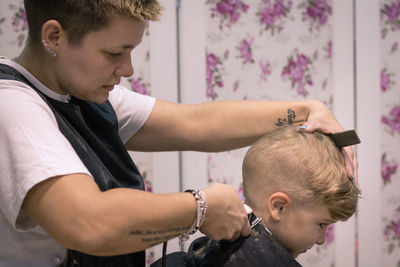 Side view of barber cutting boy hair in salon